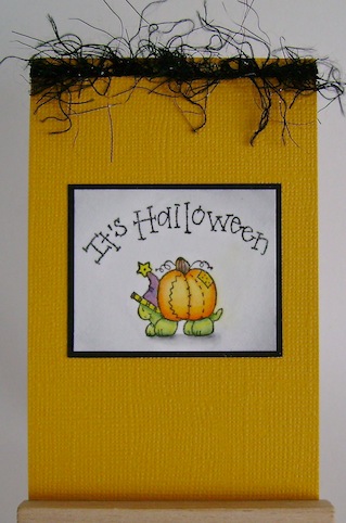 an orange card with black fuzzy ribbon at the top, a turtle carrying a pumpkin on its back and a sentiment that reads it's halloween