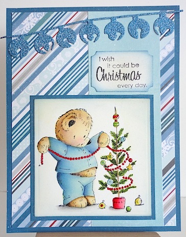 pennyblackiwishitcouldbechristmas christmas card with teddy in blue pyjamas decorating a tree; background papers are blue diagonal stripes with white and red plus a die cut strand of blue glitter jingle bells