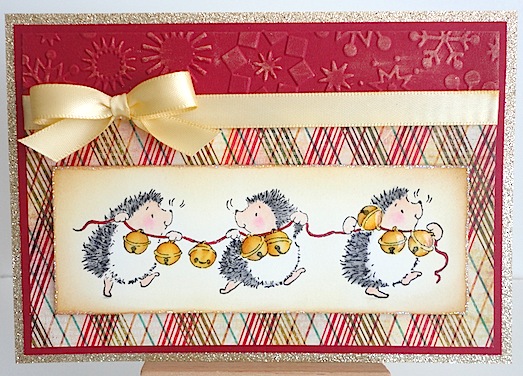 christmas card with three hedgies running along carrying a string of jingle bells on and red and brown plaid background with red card stock and gold bow