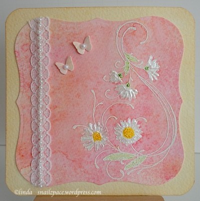 card with white daisies on a pink background with lace and pearls and two tiny butterflies