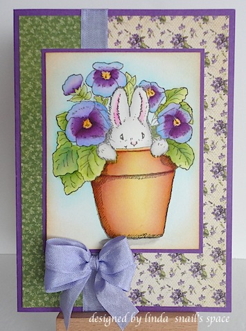 card with white bunny in a clay pot of purple pansies with green and purple print patterned paper and a purple bow