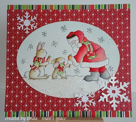 christmas card with santa handing carrots to two brown bunnies wearing scarves coloured in green and red