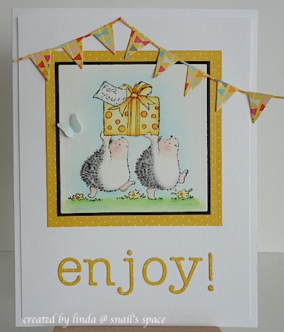 card with two hedgehogs carrying a present, a die cut enjoy sentiment and two die cut pennant borders at the top