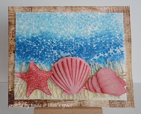 card with beach scene and sea shells in burgundy on a beige mesh ribbon with water and sky in the background