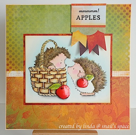 COPYRIGHT LINDA @ SNAIL'S SPACE and described here solely for people with disabilities; an autumn card with orange, red and green background papers, some banners at the top with a sentiment, "mmmmm! apples" and a watercoloured image of two hedgies with apples, one hedgie in a basket